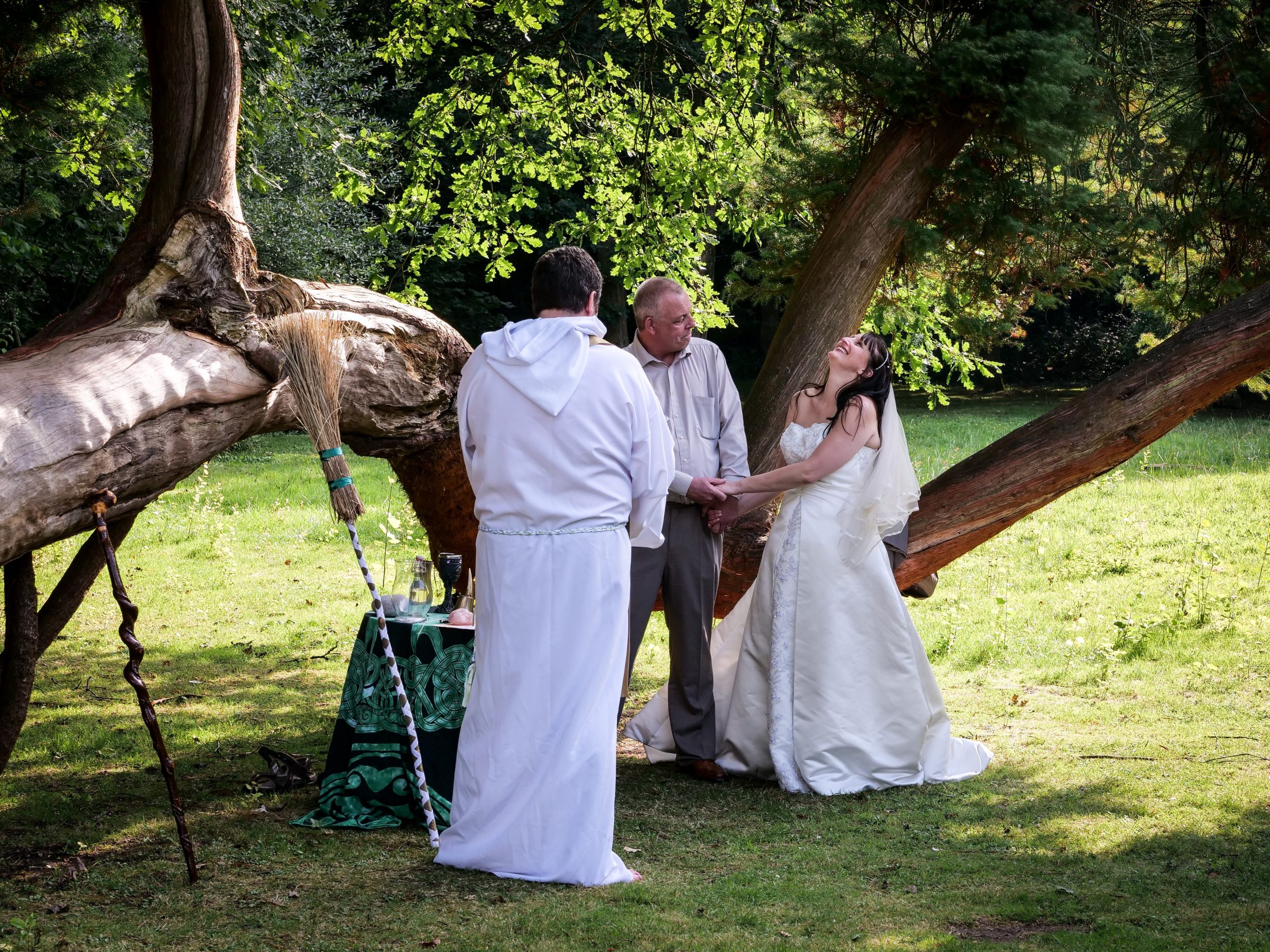 The bride throws her head back laughing during a pagan ceremony while the groom and the officiating druid look on.