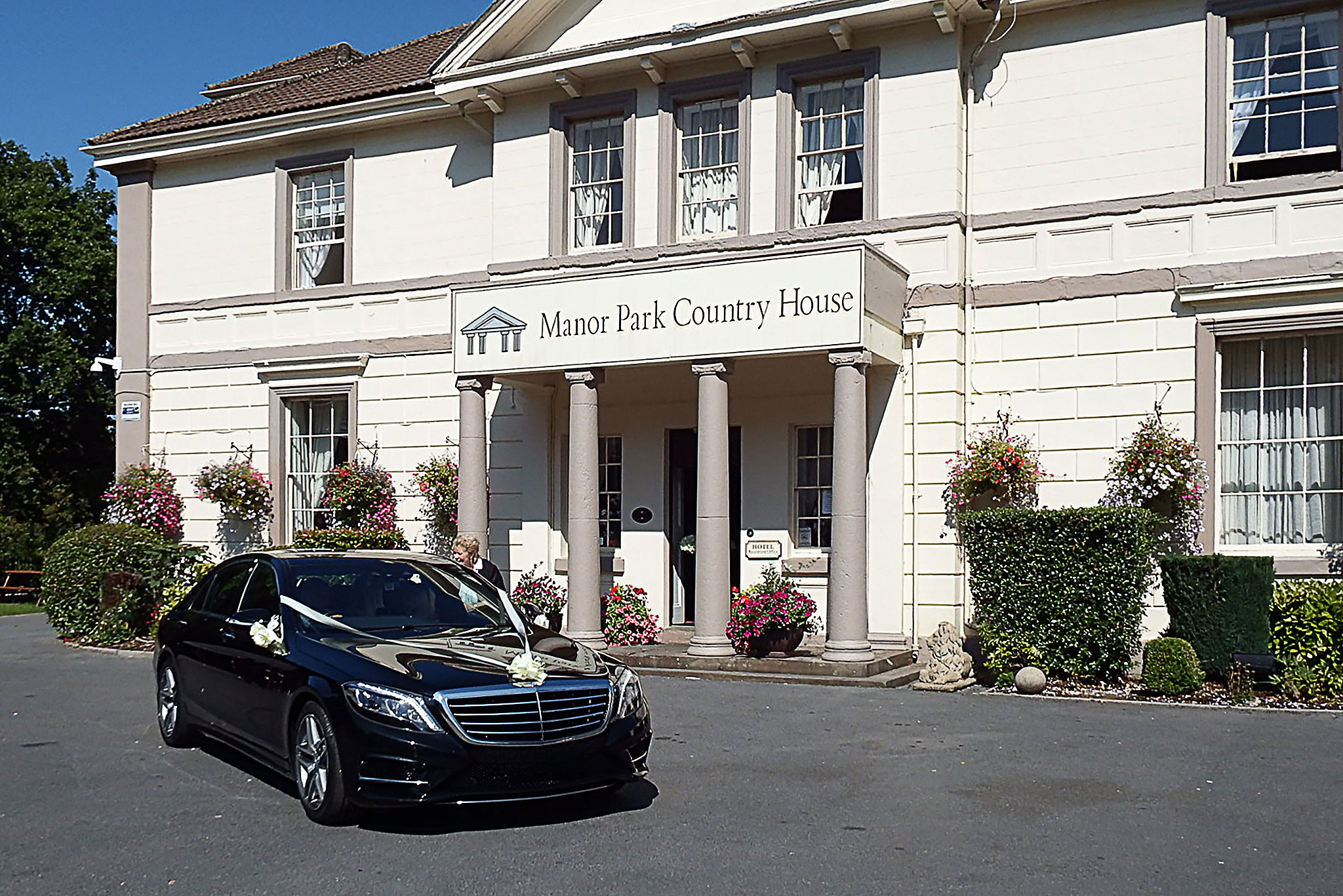 Black wedding car decorated with white ribbons parked outside Manor Park Country House in South Wales